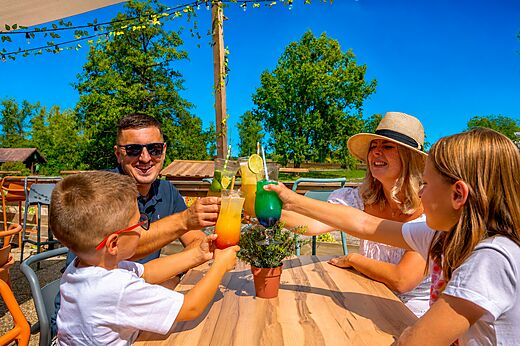 Familia sonriente brindando con cócteles coloridos en el bar del camping CLICOCHIC Etang de la Mutche en HARPRICH (57).