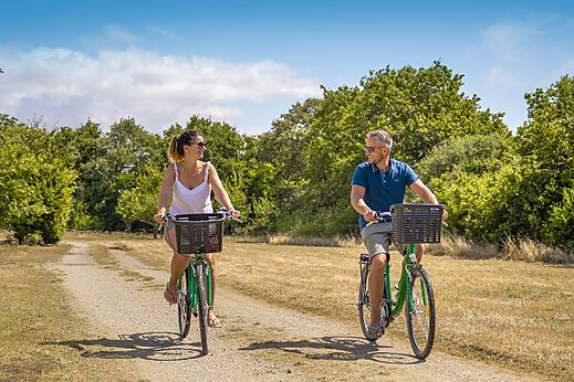 Pareja sonriente en bicicleta por camino en el camping CLICOCHIC Etoile de Mer en Asserac