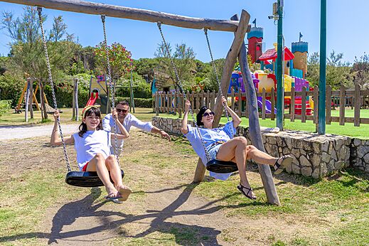 Familia sonriente en los columpios del parque infantil en el camping CAPFUN Europing en Tarquinia (01).