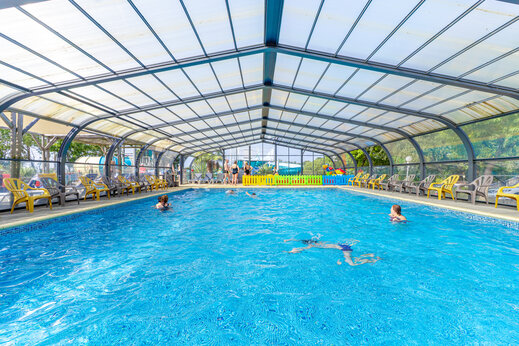 Piscina cubierta climatizada con bañistas y sillas en el camping CAPFUN L'Eve en Saint-Marc-sur-Mer (44).