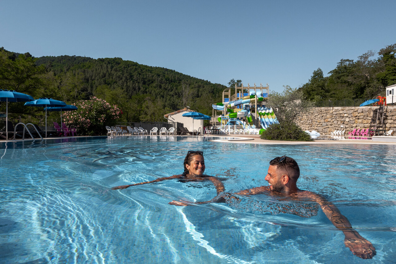 Piscina exterior con toboganes acu�ticos y pareja sonriente en el camping CLICOCHIC Eyrieux en Les OLLIERES-SUR-EYRIEUX.