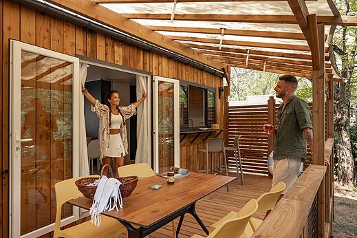 Mobil-home moderno con gran terraza de madera y pareja sonriente en el camping CLICOCHIC Eyrieux en Les OLLIERES-SUR-EYRIEUX.