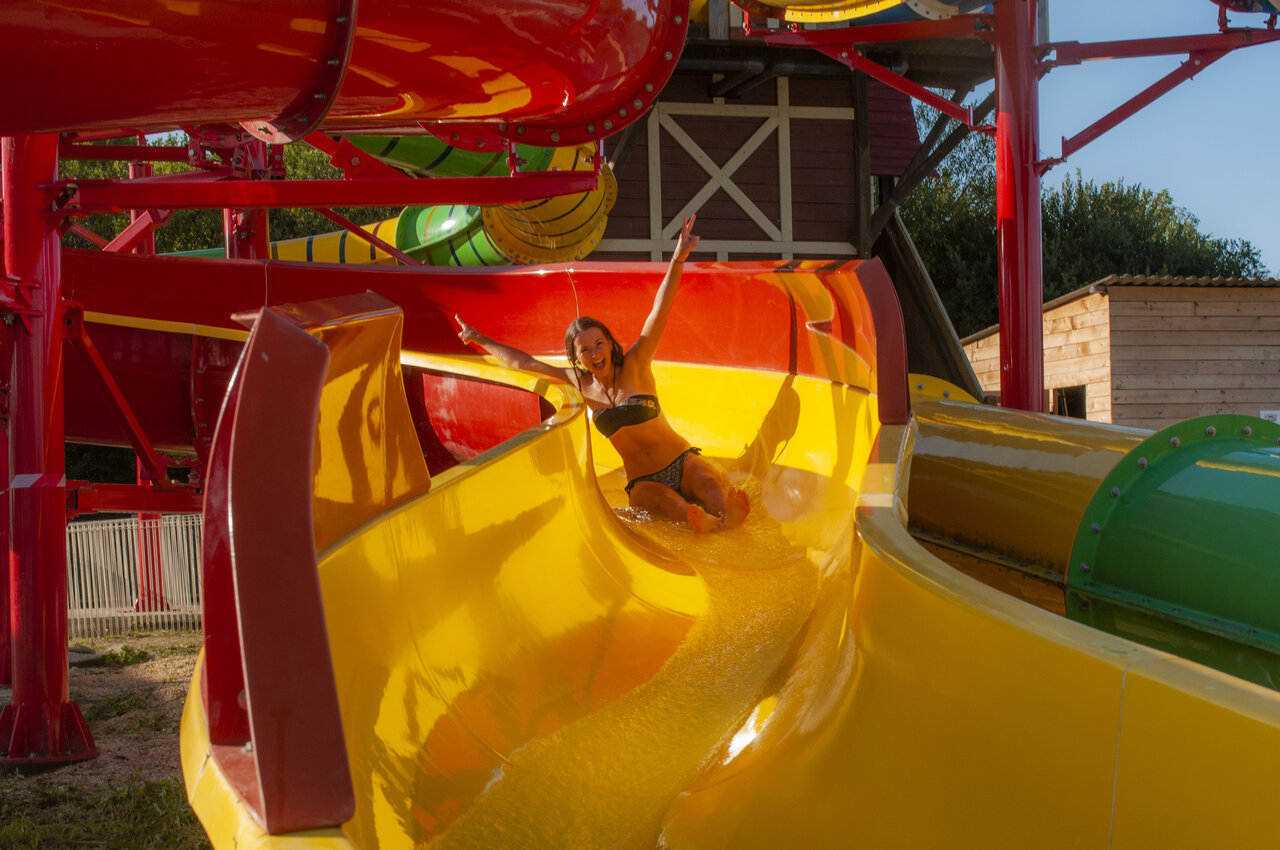 Mujer sonriente bajando por un tobog�n acu�tico amarillo en el camping CAPFUN Falaises en Gonneville sur Mer.