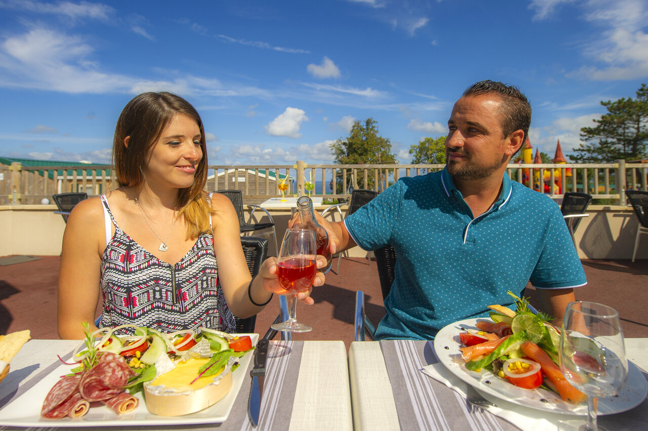 Pareja almorzando en terraza en el restaurante del camping CAPFUN Falaises en Gonneville sur Mer (14).