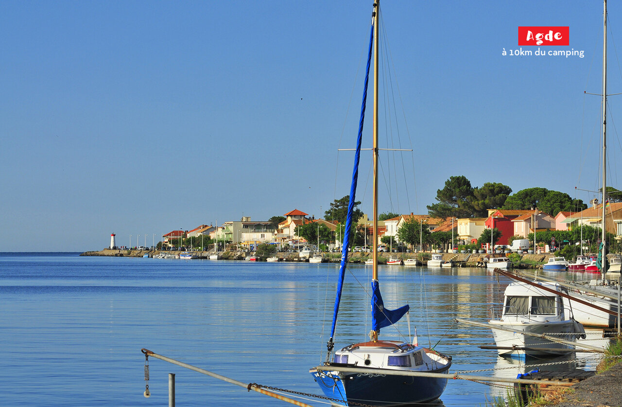 Puerto de Agde con veleros, casas coloridas y faro, para visitar cerca de Marseillan Plage.