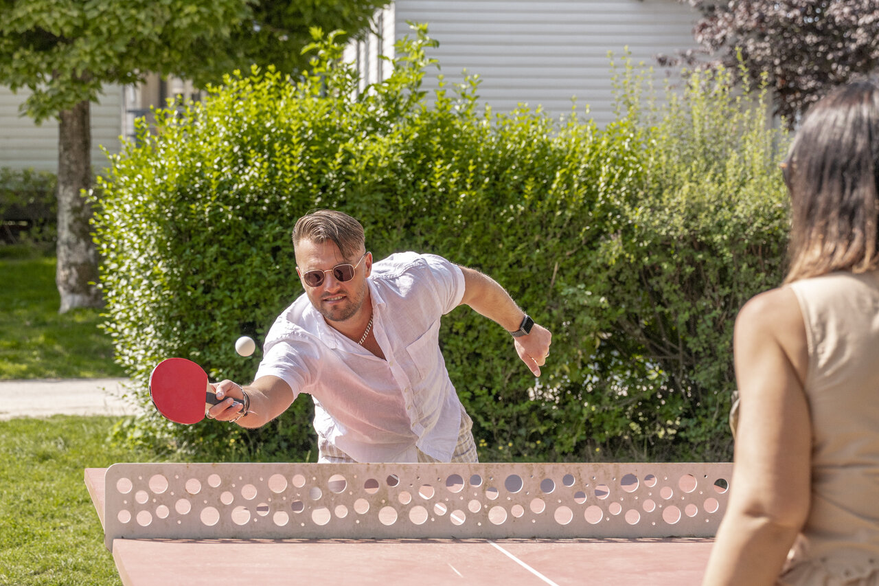 Pareja jugando al tenis de mesa al aire libre en el camping CLICOCHIC Ferme des Aulnes.