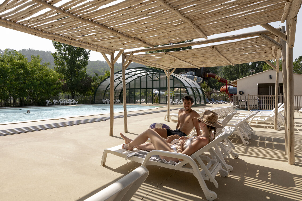 Pareja relaj�ndose junto a la piscina con toboganes en el camping CLICOCHIC Filament en Thoiras (30).