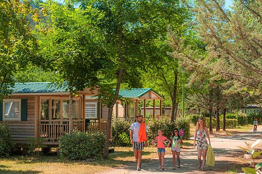 Mobil-homes de madera y familia caminando por un sendero en el camping CLICOCHIC Filament en Thoiras (30).