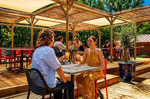 Pareja sonriente disfrutando cócteles en la terraza del bar en el camping CLICOCHIC Filament en Thoiras (30).