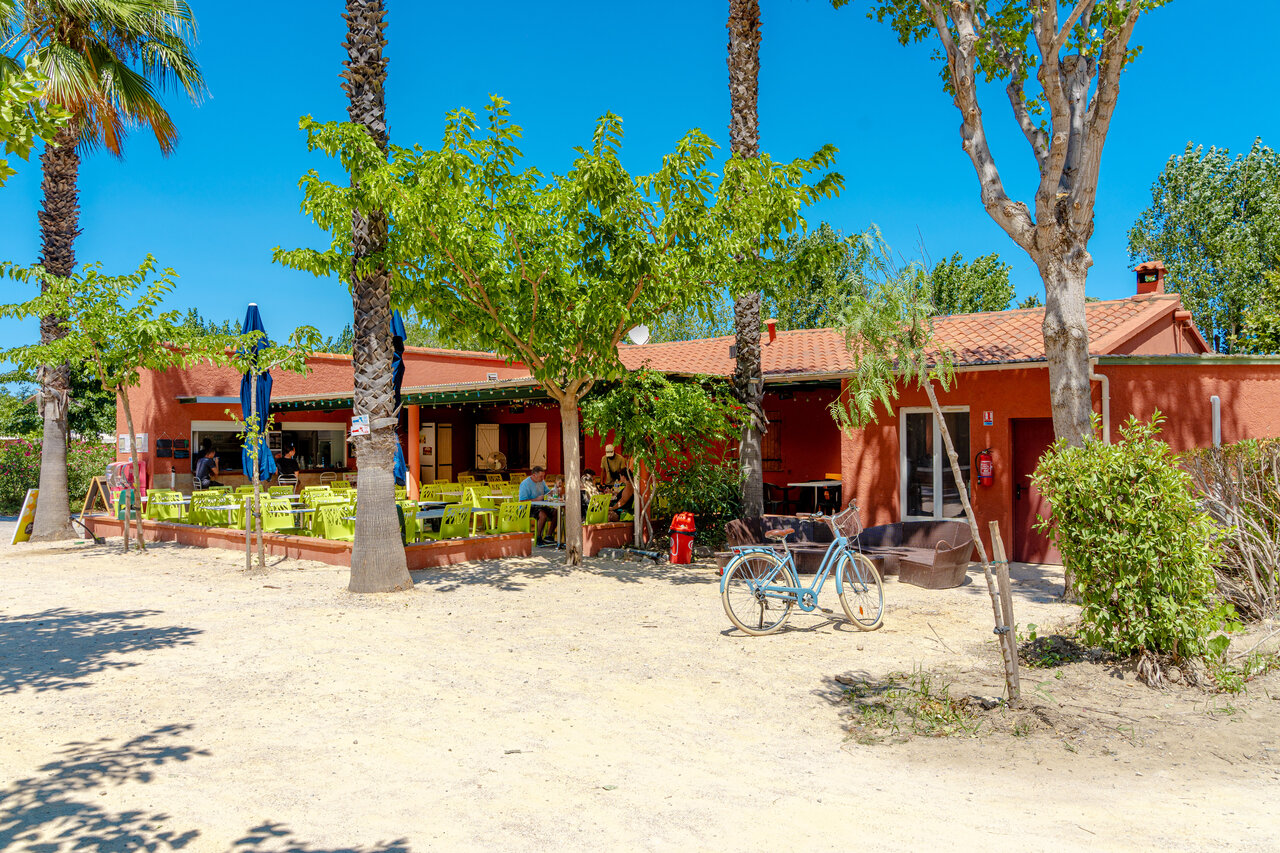 Terraza exterior del restaurante-bar con palmeras en camping VAGUES OCEANES Au Flamenco Argel�s-sur-Mer.