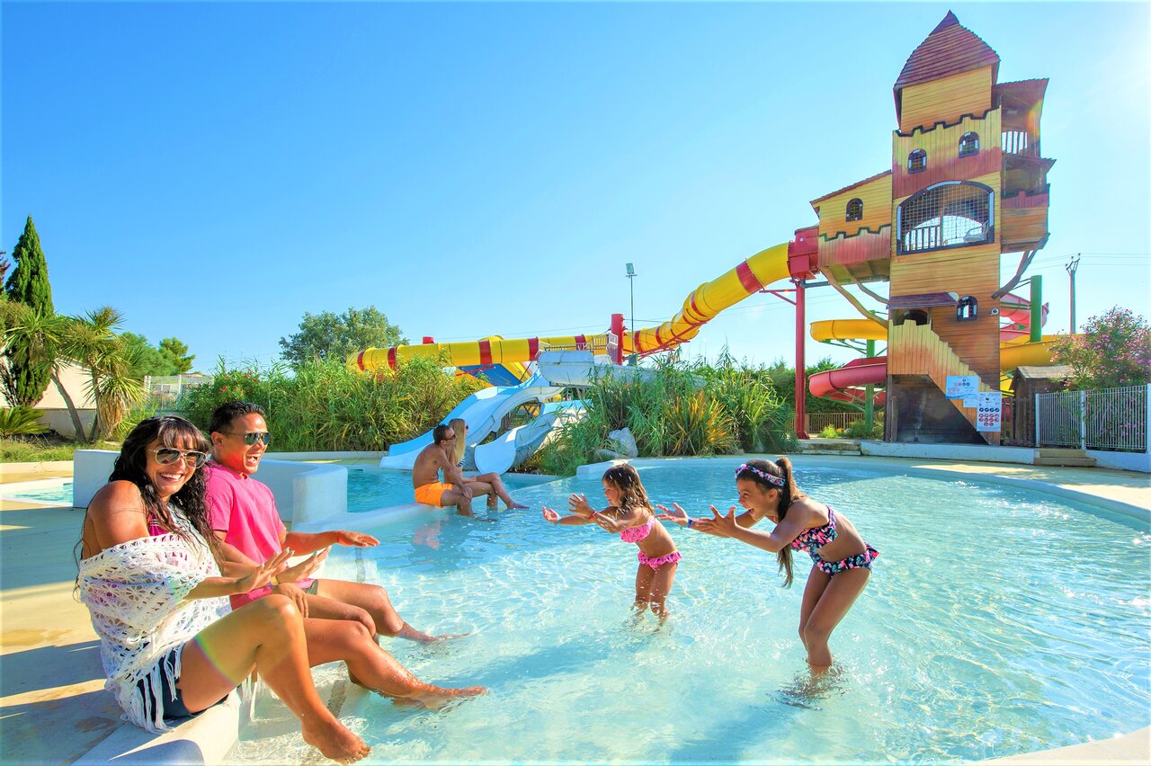 Piscina con toboganes acu�ticos, estructura de castillo y familia en el camping CAPFUN Fleur de Camargue en Saint-Laurent-d Aigouze (30).