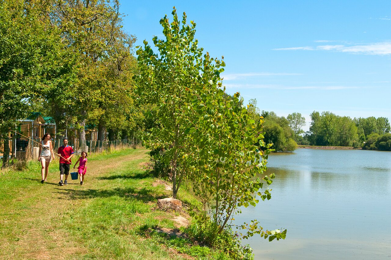 Familia pescando junto al lago, alojamientos al fondo en el camping CAPFUN Forges en Avrille (85).