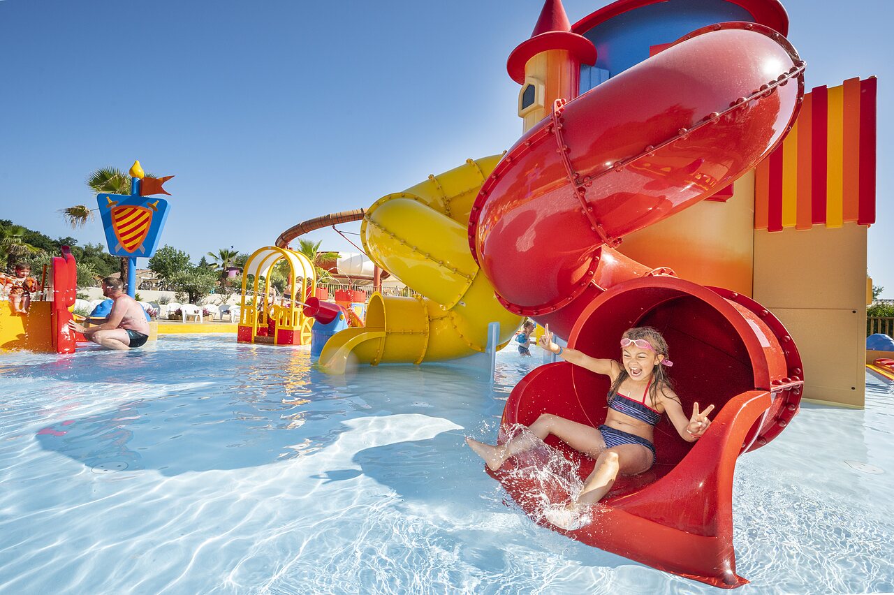 Ni�a sonriente bajando por un tobog�n acu�tico rojo en la piscina del camping CAPFUN Forges en Avrille (85).
