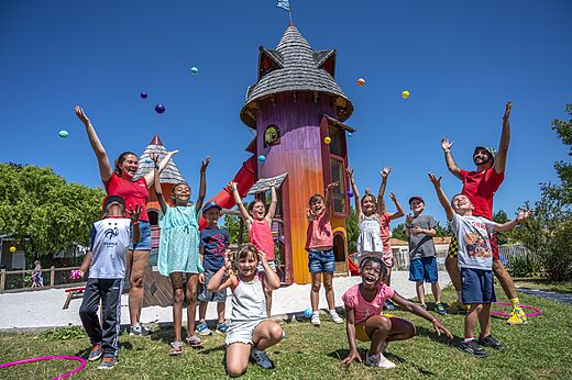 Niños felices jugando con animadores cerca de una torre de juegos en el camping CAPFUN Forges en Avrille (85).