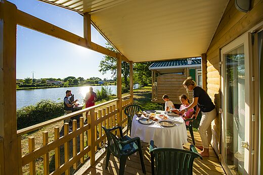 Terraza de Mobil-home, familia comiendo, barbacoa junto al lago en el camping CAPFUN Forges en Avrille (85).