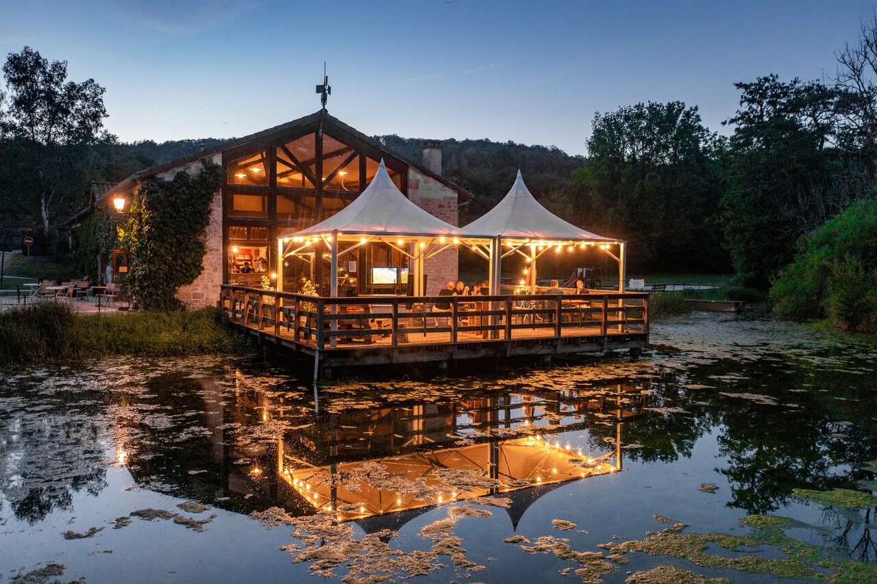 Restaurante y bar iluminados sobre pont�n en el camping CLICOCHIC Forge Sainte Marie.