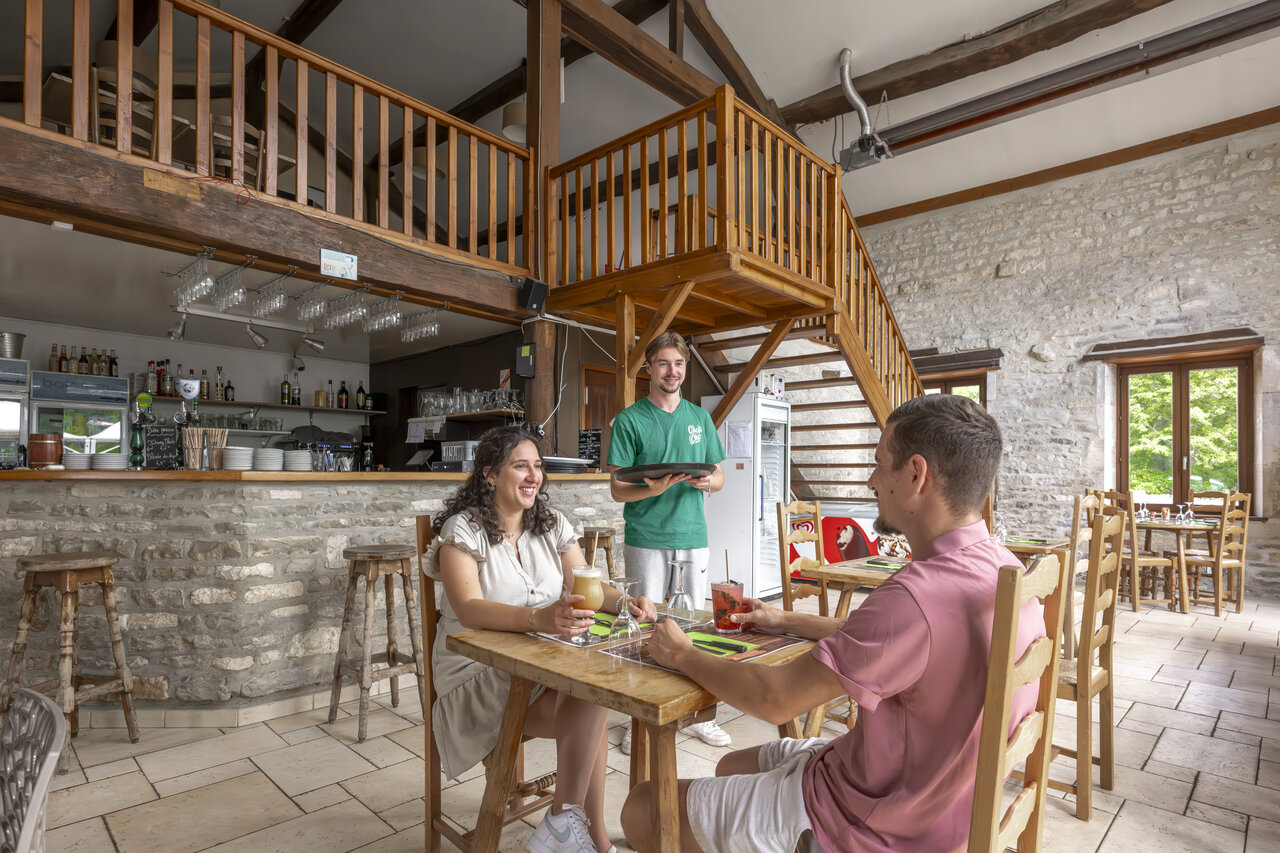 Interior restaurante-bar, pareja y camarero en camping CLICOCHIC Forge Sainte Marie Thonnance-les-Moulins.