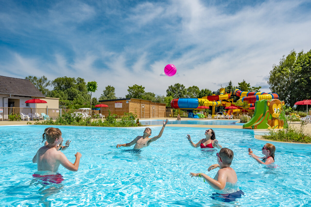 Familia jugando con pelota en piscina con toboganes en camping CAPFUN Fort Falabraque en Seltz (67).
