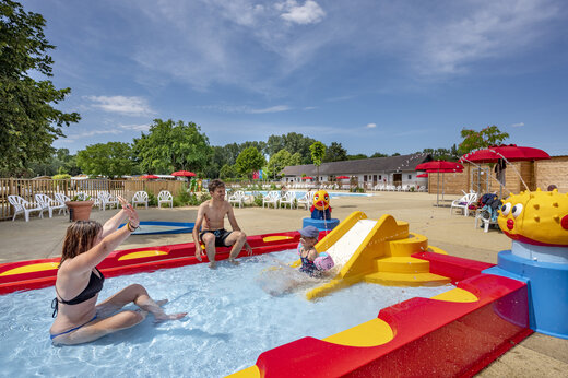 Zona de juegos acuáticos con tobogán y familia en el camping CAPFUN Fort Falabraque en Seltz (67).