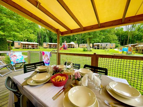 Mobil-home con terraza, mesa puesta y juegos infantiles en el camping CAPFUN Fredland en Tournan en Brie.