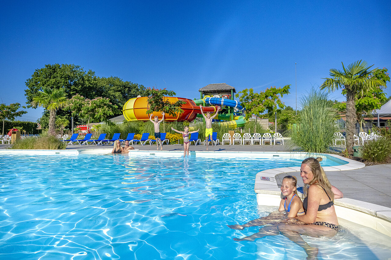 Piscina exterior con toboganes acu�ticos y familia feliz en el camping CAPFUN De Fruithof en Klijndijk.