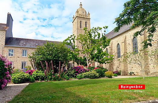 Iglesia histórica de Bricquebec con campanario y jardín florido en Normandía.