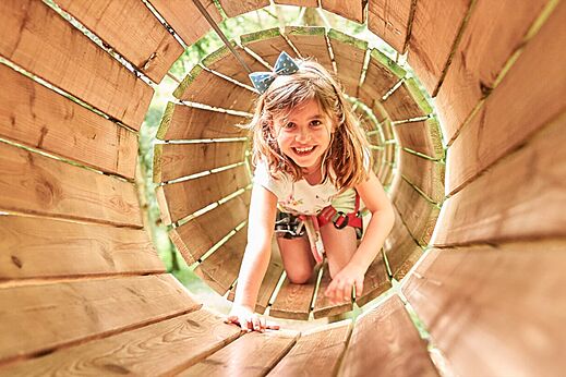 Niña sonriente en túnel de madera, recorrido de aventura, camping CAPFUN Grand Cerf en Gimouille.