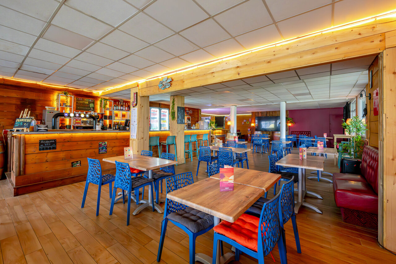 Bar y zona de restaurante con mesas y sillas en el camping CAPFUN Grand Large en FOUESNANT (29).