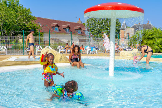 Niños jugando en la piscina con seta rociadora en el camping CAPFUN Grenouillère en Suèvres (41).