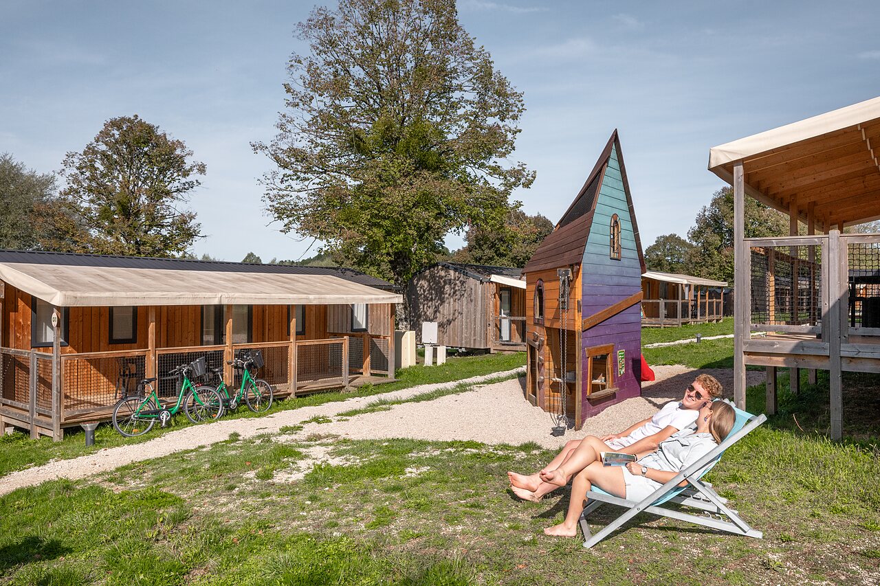 Pareja relaj�ndose junto a caba�as y zona de juegos en camping CLICOCHIC Grisi�re en Clairvaux-les-Lacs (39).