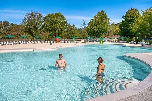 Gran piscina exterior con sillas y sombrillas en el camping CLICOCHIC Grisière en Clairvaux-les-Lacs (39).