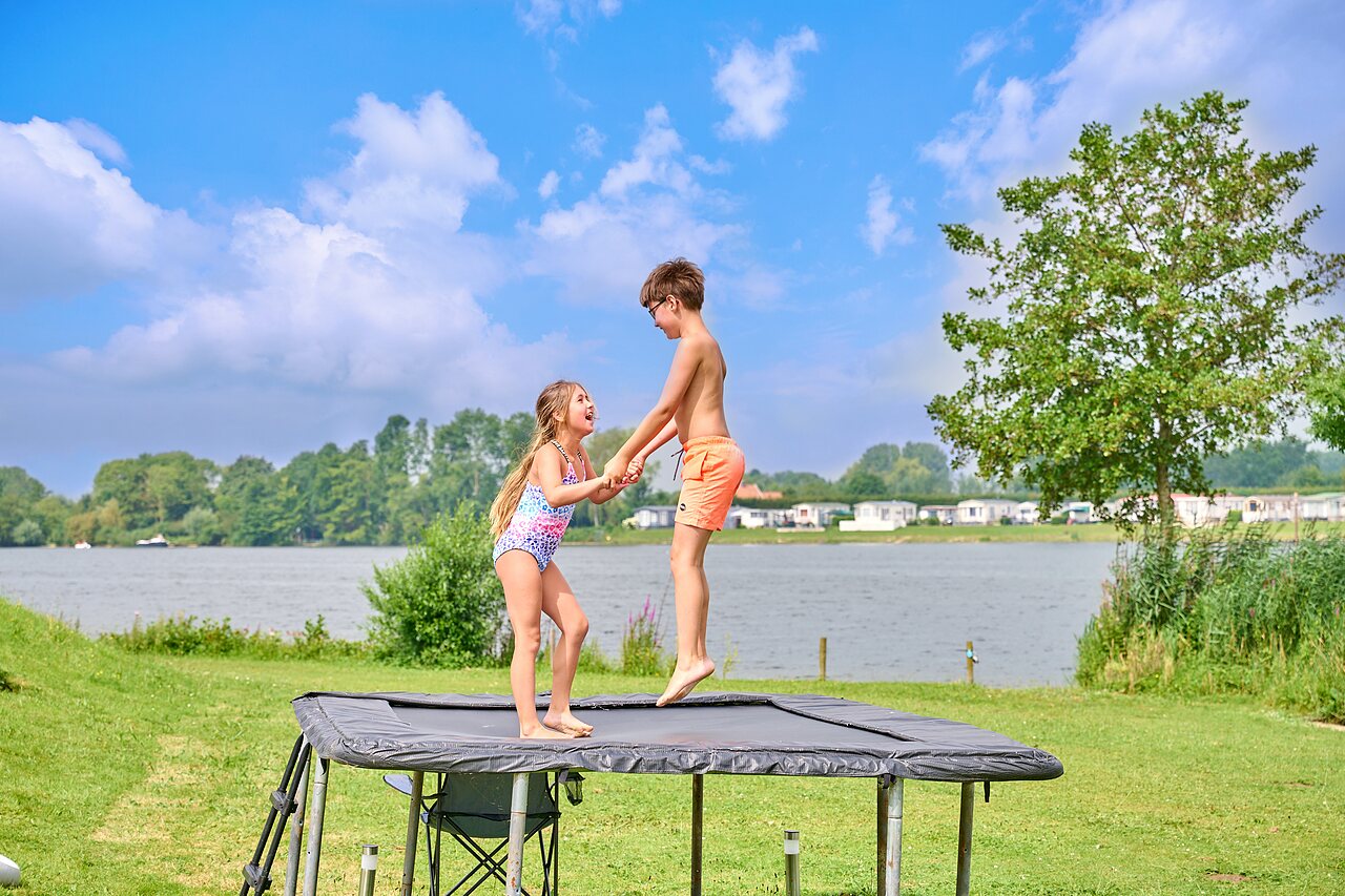 Dos ni�os saltando en trampol�n exterior junto al lago en el camping CAPFUN Groene Eiland en Appeltern.