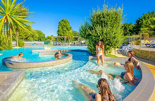 Piscina exterior con chorros y bañistas en el camping VAGUES OCEANES Grosses Pierres en Saint-Georges-d'Oléron (17).