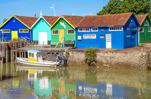 Cabañas ostrícolas coloridas y barco de pesca en un pueblo típico de Charente-Maritime.