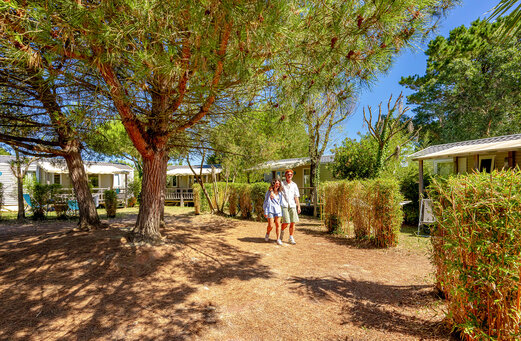 Camino sombreado con Mobil-homes y pareja en el camping VAGUES OCEANES Grosses Pierres en Saint-Georges-d'Oléron (17).