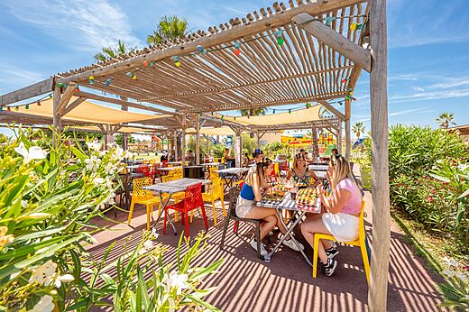 Terraza de restaurante exterior animada con comensales en el camping VAGUES OCEANES Hamacs en Fleury (11).