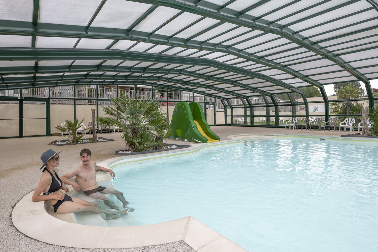 Piscina cubierta con tobog�n cocodrilo y pareja en el camping CLICOCHIC Haras de Deauville en Touques (14).