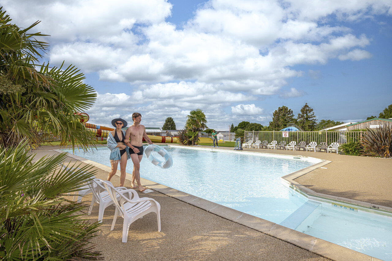 Pareja en piscina exterior con toboganes en camping CLICOCHIC Haras de Deauville.