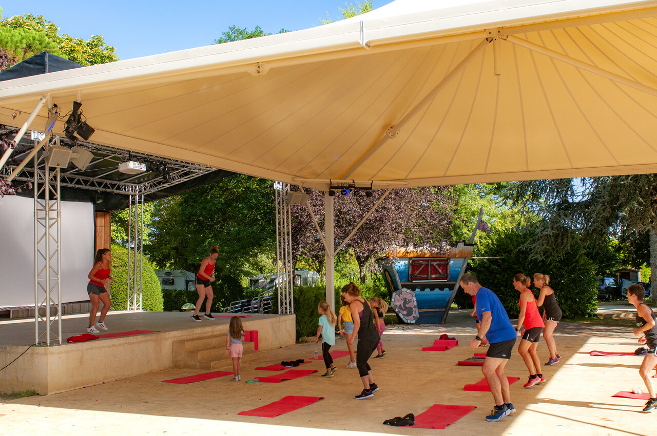 Clase de fitness al aire libre en escenario cubierto en el camping CAPFUN Hauts de Ratebout en STE FOY DE BELVES (24).