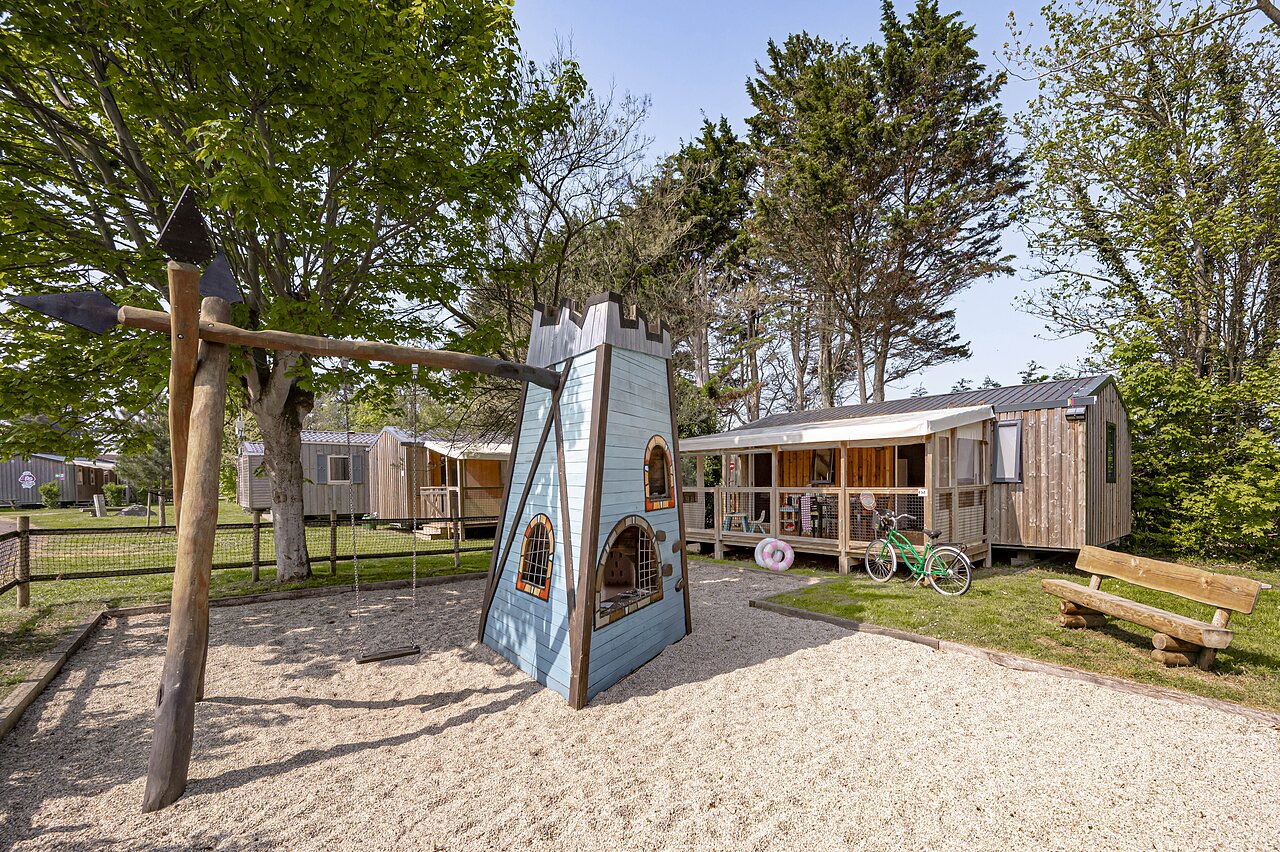 Zona de juegos infantil con castillo y columpio, mobil-homes en camping CLICOCHIC Havre de Berni�res en Berni�res-sur-Mer (14).