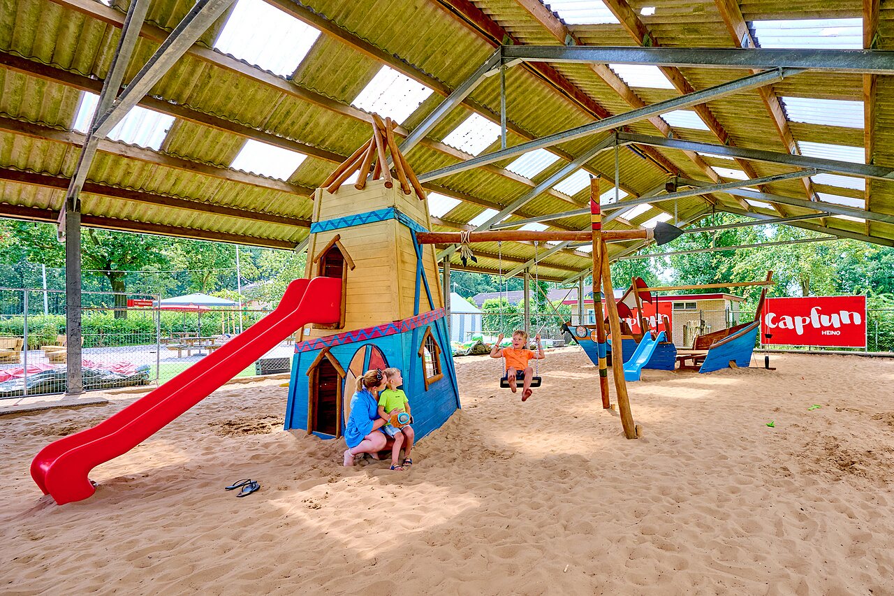 Zona de juegos cubierta con tobog�n, columpios y arena en el camping CAPFUN Heino en Heino.