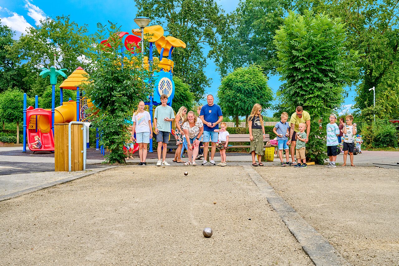 Familia jugando petanca cerca de parque infantil en camping CAPFUN Heino en Heino.