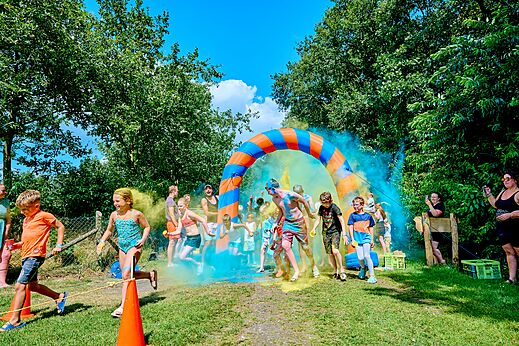 Niños y adultos en carrera de colores bajo arco inflable en camping CAPFUN Heino en Heino.