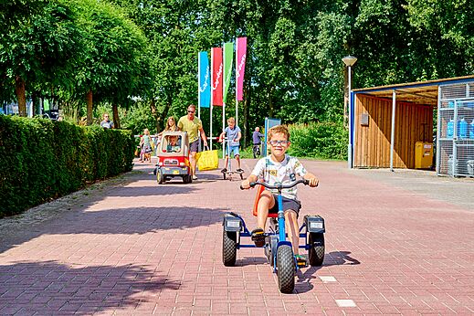 Niños jugando con kart a pedales, coche de juguete y patinete en camping CAPFUN Heino en Heino.