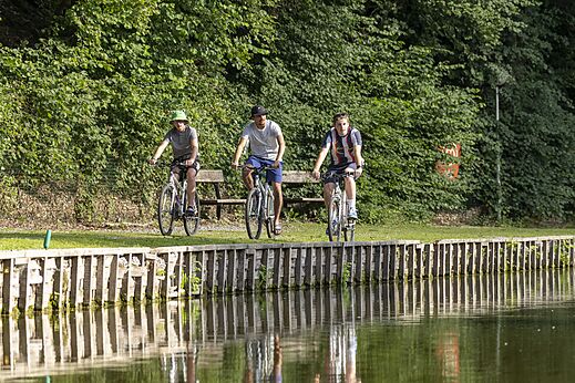 Tres personas en bicicleta junto a un curso de agua en el camping CAPFUN Hirondelle en Oteppe.
