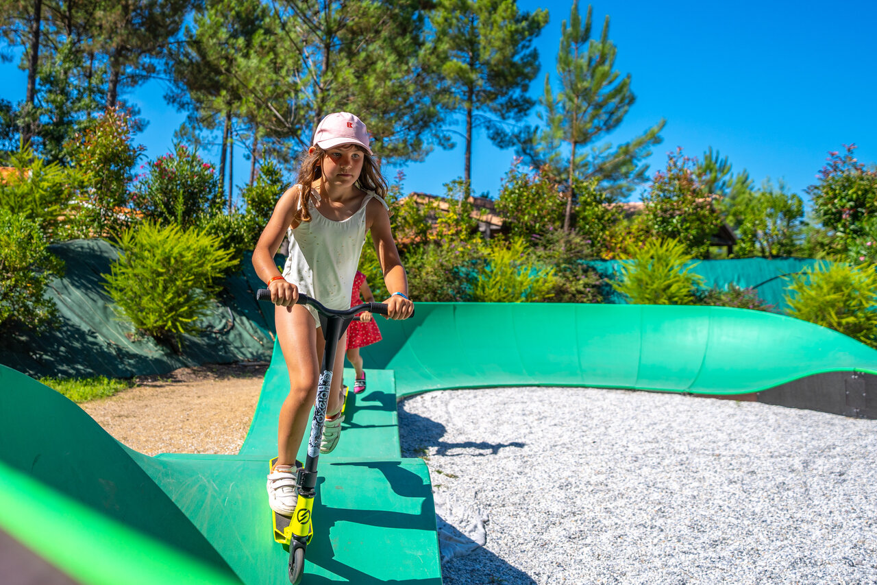 Ni�a en patinete sobre pumptrack verde en el camping CAPFUN Huttes en Saint-Denis d'Ol�ron.