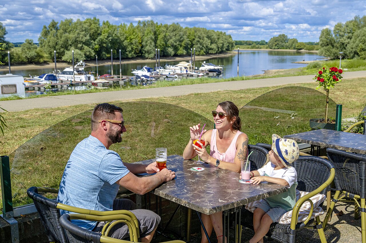 Familia sonriente tomando bebidas en terraza junto a puerto deportivo en camping CAPFUN IJsselstrand en Doesburg.