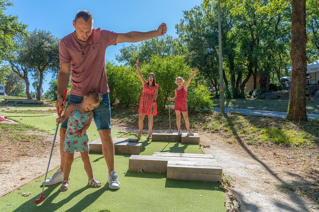 Familia jugando minigolf en campo exterior en camping CAPFUN Imbours en LARNAS (07).