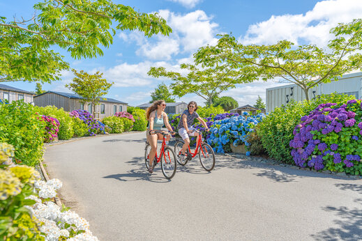 Dos personas en bicicleta por camino florido en camping CAPFUN Kervel en PLONEVEZ PORZAY (29).