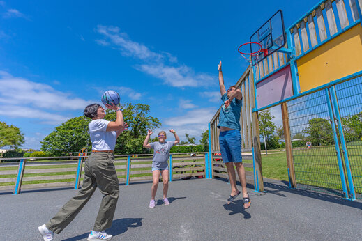 Familia jugando al baloncesto en la cancha multideporte del camping CAPFUN Kervel en PLONEVEZ PORZAY (29).